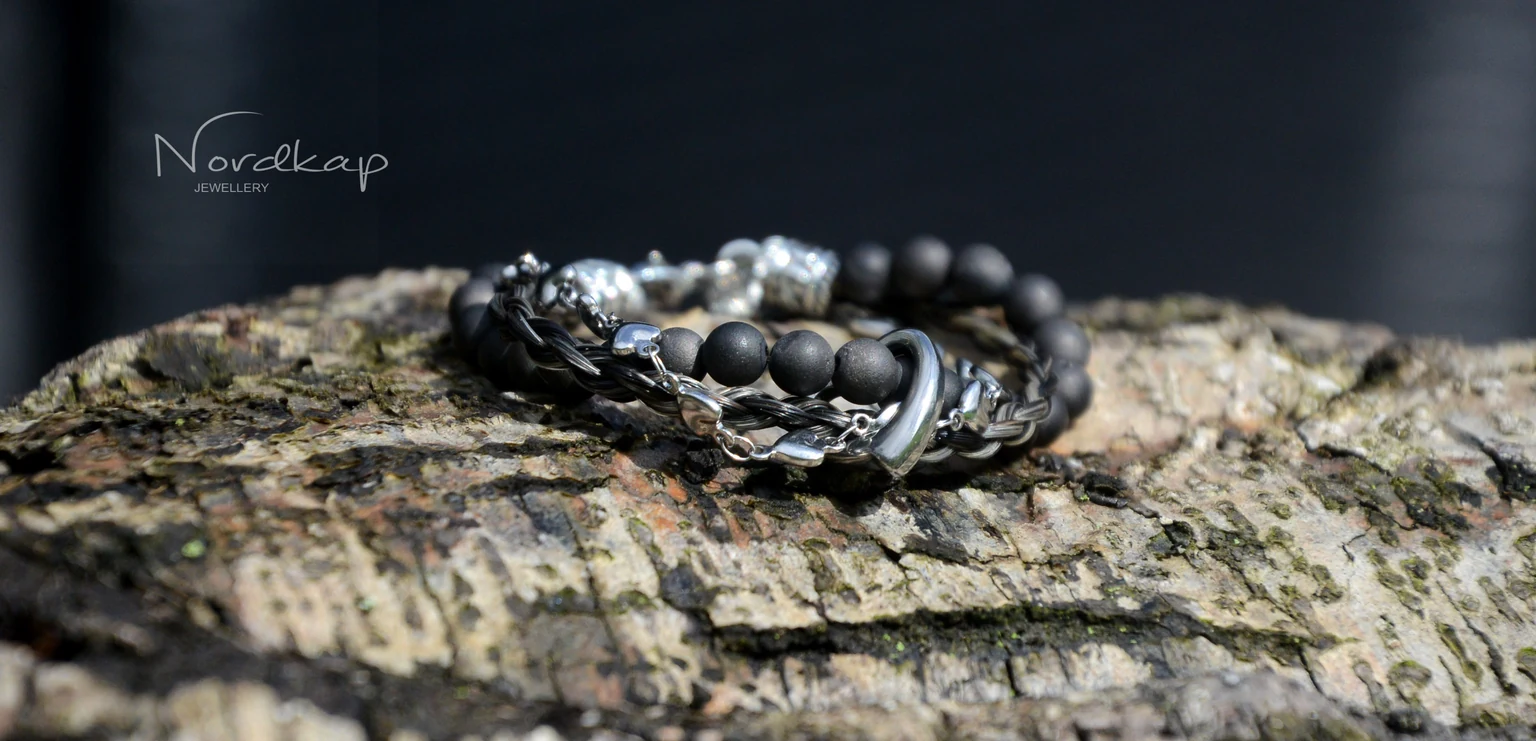 Armband aus schwarzem Pferdehaar mit dunklen Perlen und silberfarbener Kette auf Rinde